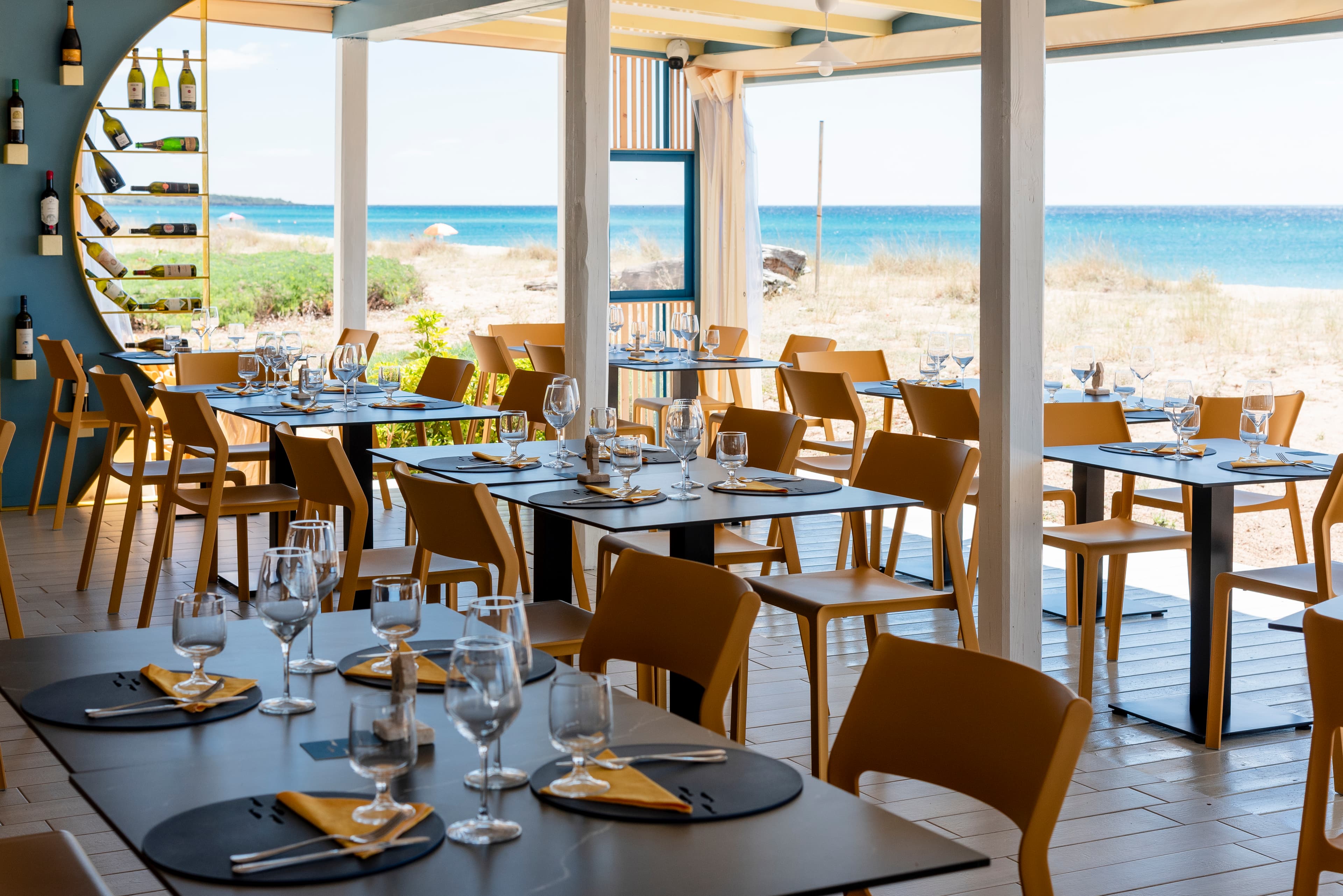 Sala del Lungomare con tavoli apparecchiati e il mare davanti alla spiaggia.