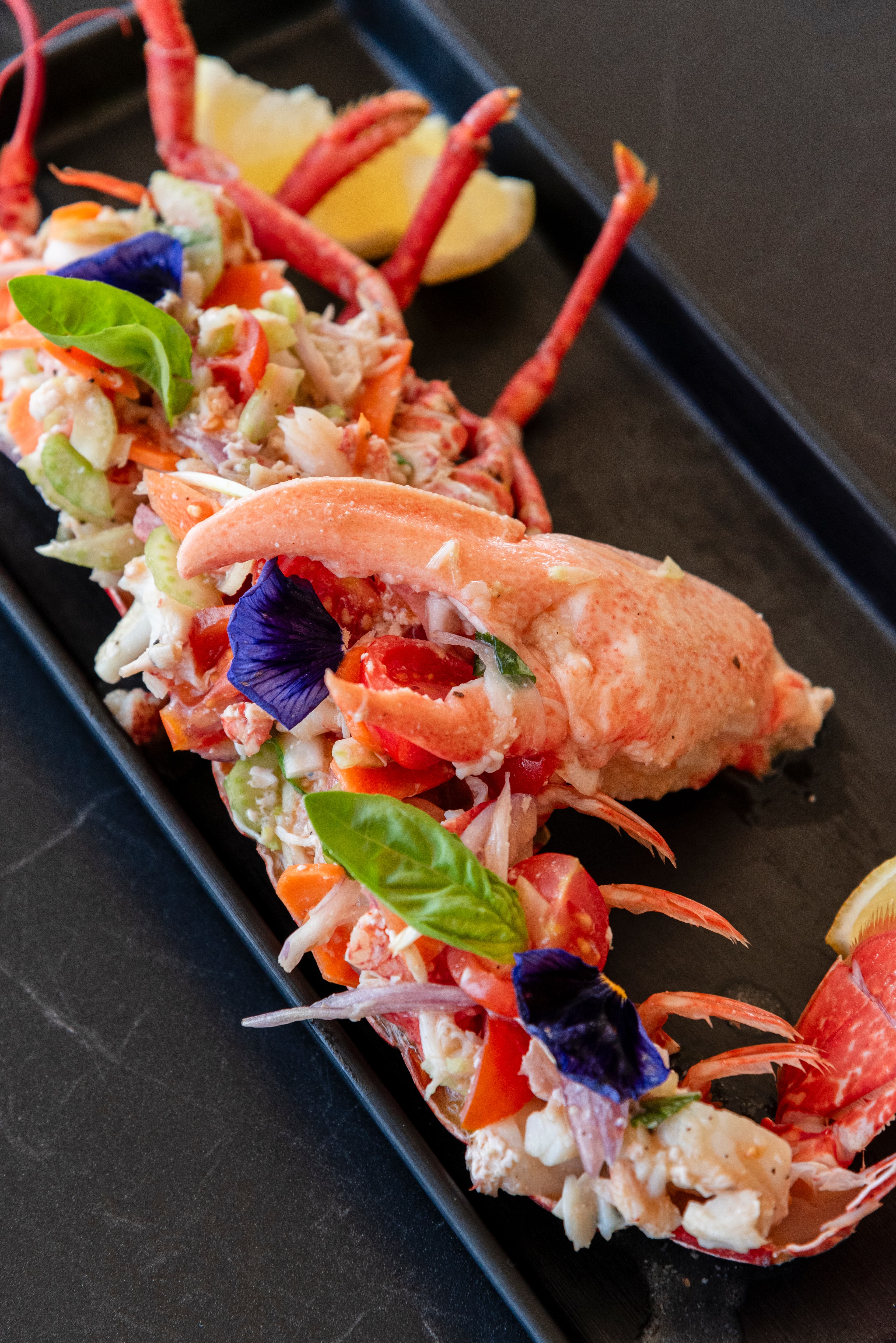 Bogavante servido con tomate y ensalada en un plato vertical.